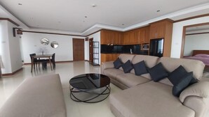 Un salon moderne avec un canapé beige, une table basse en verre et un coin repas comprenant une table et des chaises.
