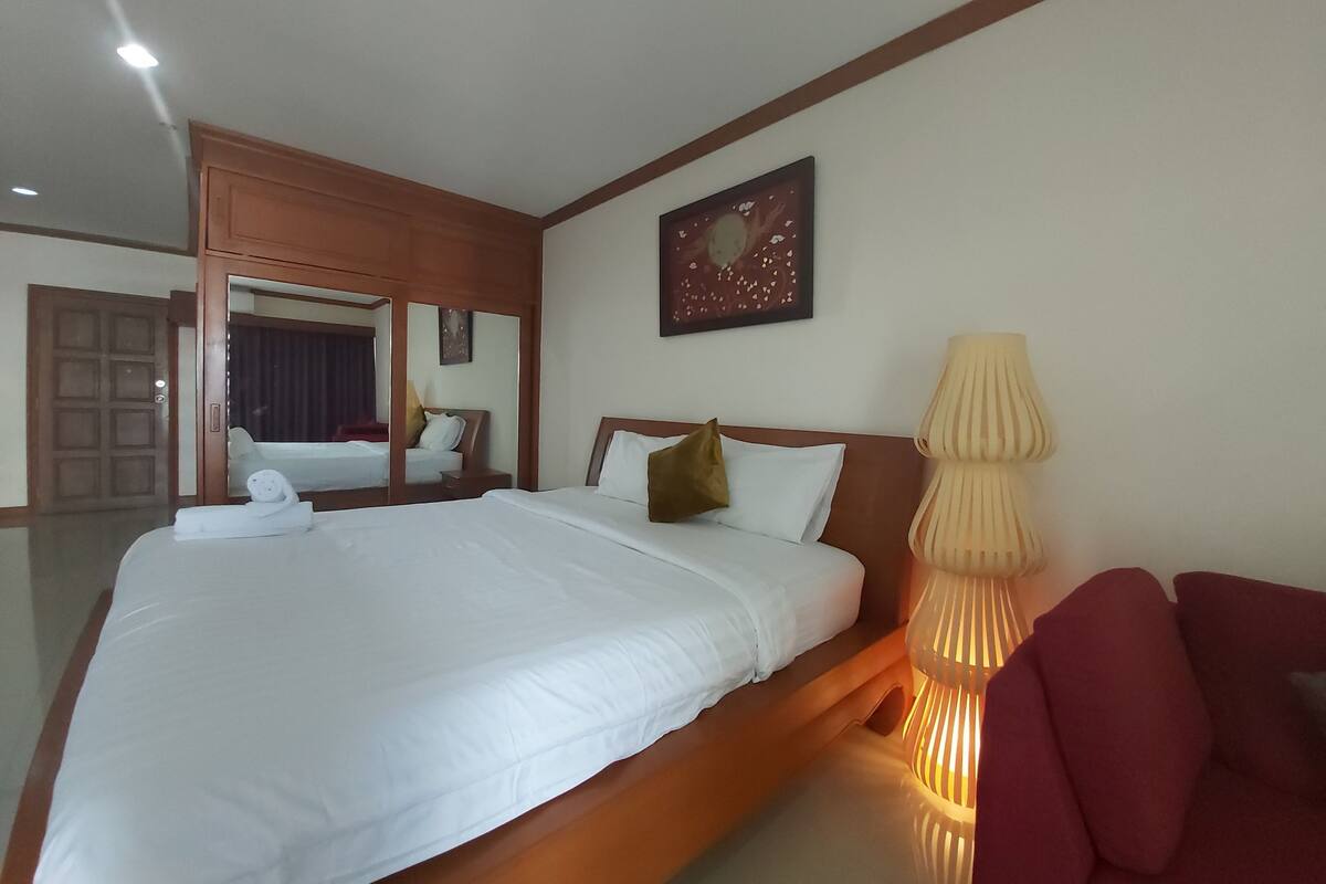 Une chambre d’hôtel avec un grand lit, une lampe de chevet, un miroir et une chaise rouge.