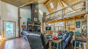 A spacious living area with a fireplace, leather sofas, and a high ceiling with exposed beams. - Wild Horse Lodge | Galloping Good Times Retreat w/ Game room Fun & Spacious Living (Alto)