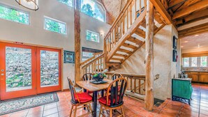 A spacious dining area with a wooden staircase, stone walls, and a view of the outdoors. - Wild Horse Lodge | Galloping Good Times Retreat w/ Game room Fun & Spacious Living (Alto)