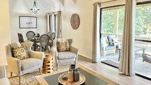 A living room with a dining area, a large clock on the wall, and a view through a glass door. - Family-Friendly or Romantic Retreat • Pools + Private Beach Access  (Miramar Beach)