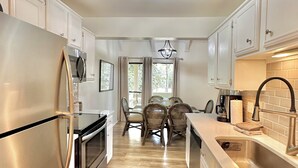 A modern kitchen with stainless steel appliances, a dining area with wicker chairs, and a view of the outdoors. - Family-Friendly or Romantic Retreat • Pools + Private Beach Access  (Miramar Beach)