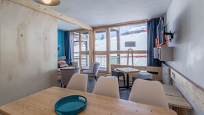 Una habitación acogedora con paredes de madera y un ventanal que da a un paisaje nevado. Hay varias sillas y una mesa con una bandeja azul.