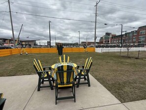 A grassy area with a table and chairs, a fence, and buildings in the background. - Game Day HQ w/ Fan Cave, Fire Pit + Stadium Views (Green Bay)