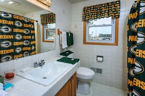 A bathroom with a large mirror, a sink, a toilet, and a window with a view of a building. - Game Day HQ w/ Fan Cave, Fire Pit + Stadium Views (Green Bay)