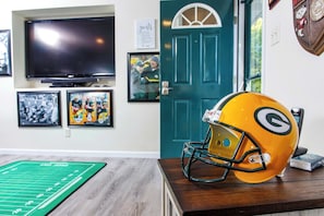 Une pièce avec un téléviseur, des tableaux encadrés accrochés au mur, une porte et un casque de football posé sur une table.