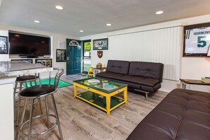Ein Wohnzimmer mit Fernseher, einer Couch, einem Couchtisch und einer Bar mit Hockern.