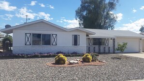 A single-story house with a white exterior, a garage, and a gravel driveway.