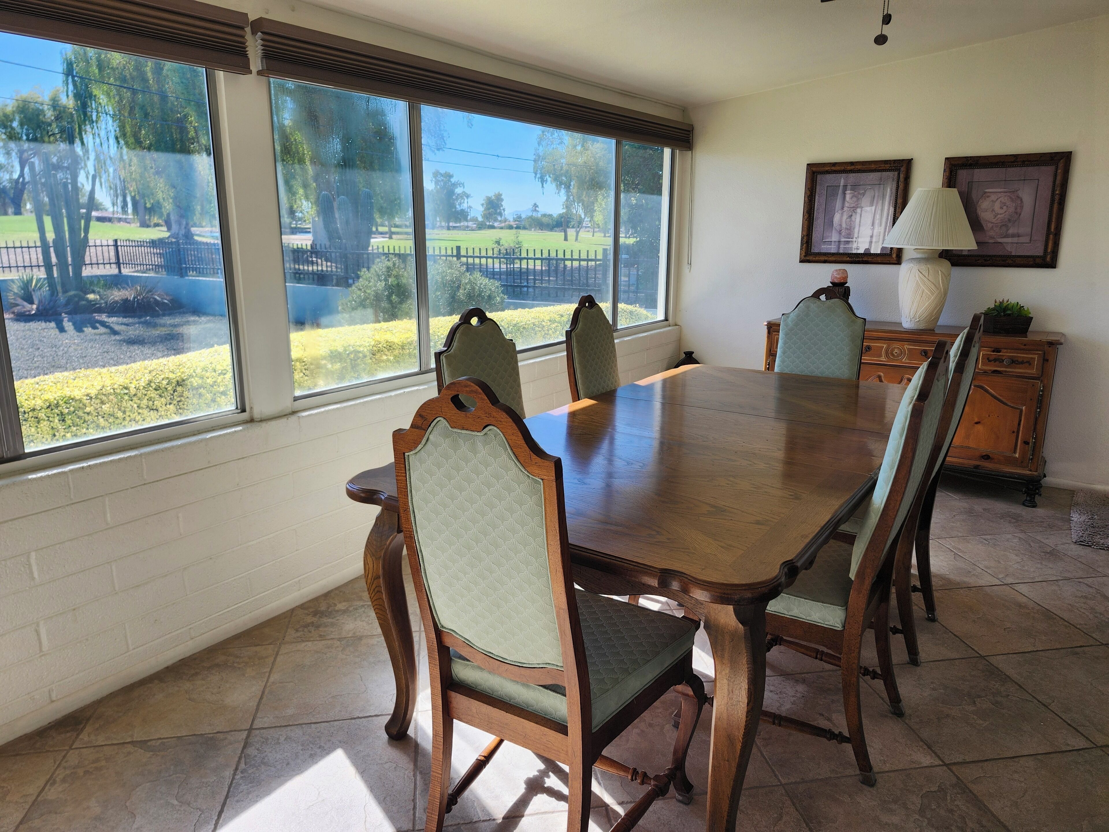 A dining room with a large wooden table and four chairs, a cabinet, and two framed pictures on the wall.