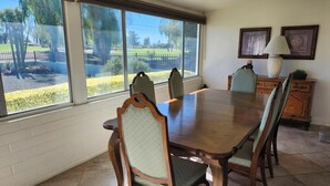 A dining room with a large wooden table and four chairs, a cabinet, and two framed pictures on the wall.
