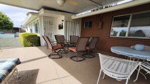 An outdoor patio with a table and chairs, a ceiling fan, and a covered area with a window.