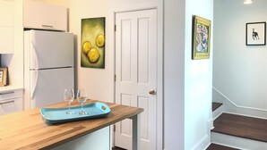 Una cocina con armarios blancos, un refrigerador blanco, una encimera de madera y una puerta con una pintura de limones. Hay dos copas de vino sobre una bandeja azul en la encimera.