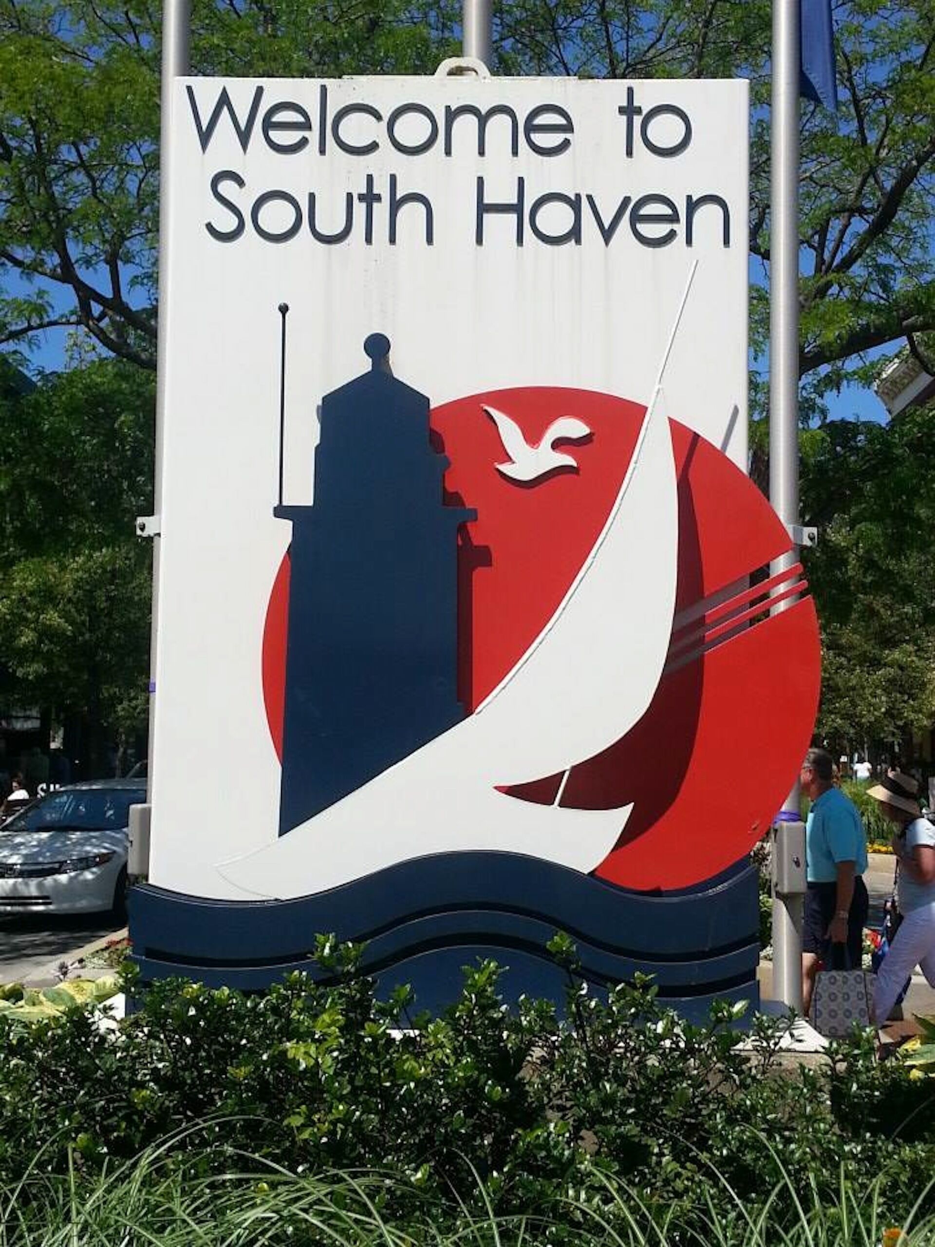 A welcome sign with a silhouette of a building and a bird, surrounded by greenery.
