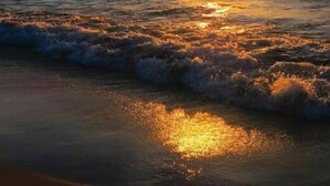 A sunset over the ocean with waves on the shore.