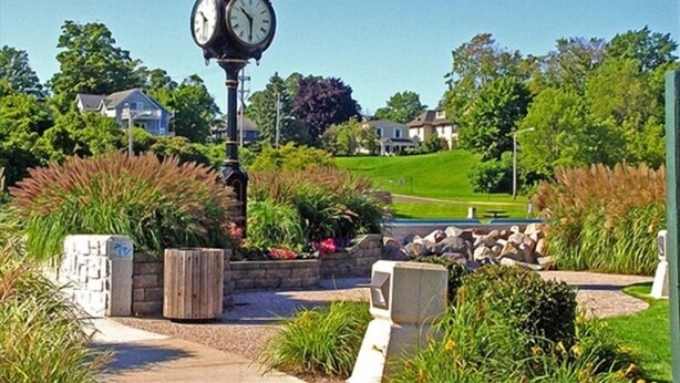 A clock tower in a landscaped area with houses in the background.