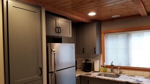 A kitchen with stainless steel appliances, wooden ceiling, and a window with blinds.