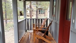 A wooden porch with a red door, a wooden chair, and a metal grate.