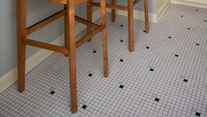 A kitchen with two wooden bar stools, a countertop, a microwave, and a tiled floor.