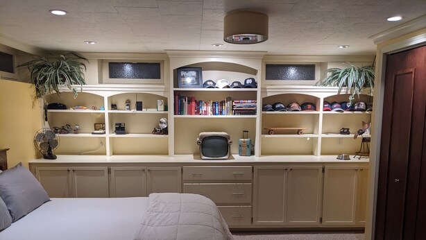 A bedroom with a bed, a desk with shelves, and a television.