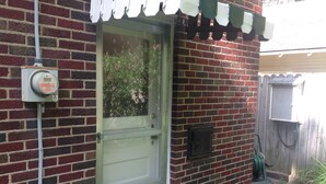 A brick house with a green door, a utility box, and a hose on the side.