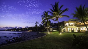 Une propriété située en bord de mer, dotée d’une pelouse bien entretenue et éclairée, de palmiers et offrant une vue sur l’océan.