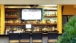 An outdoor bar area with a checkered floor, bar stools, a television screen, and shelves stocked with various bottles. - Orlando Villa Close to Disney and Free Water Park (Kissimmee)