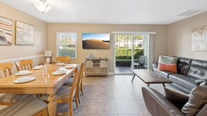 A dining area with a wooden table set for four, a sofa, and a large window with a view of a desert landscape. - Orlando Villa Close to Disney and Free Water Park (Kissimmee)