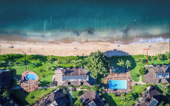 An aerial view of a beachfront property with a pool, a large building, and a designated area for a condo.