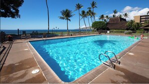 A swimming pool with clear blue water, surrounded by palm trees and a view of the ocean. - Stunning Beach Front Townhouse (Kihei)