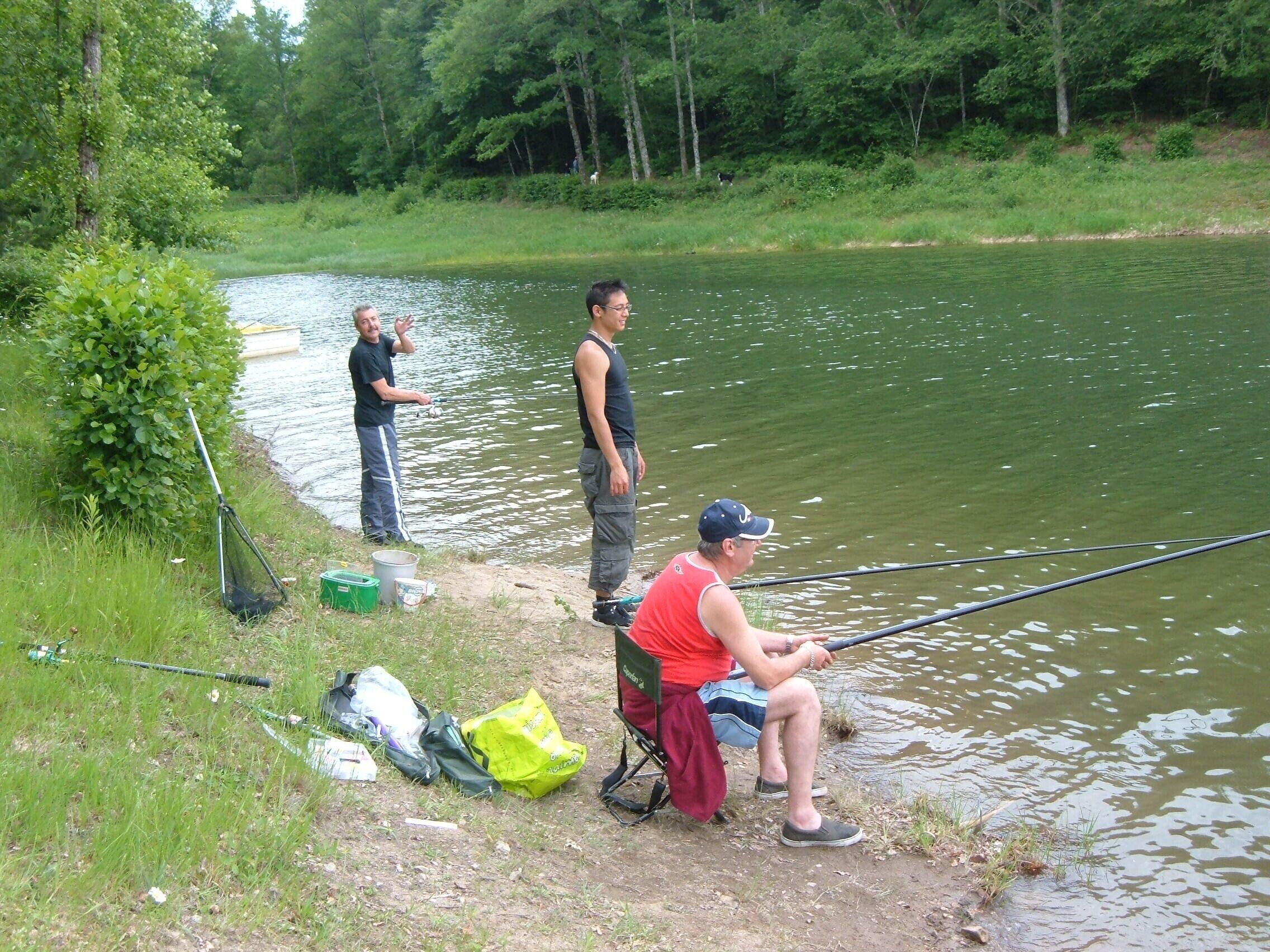 A group of people fishing by a calm river, with a boat and fishing gear on the shore.