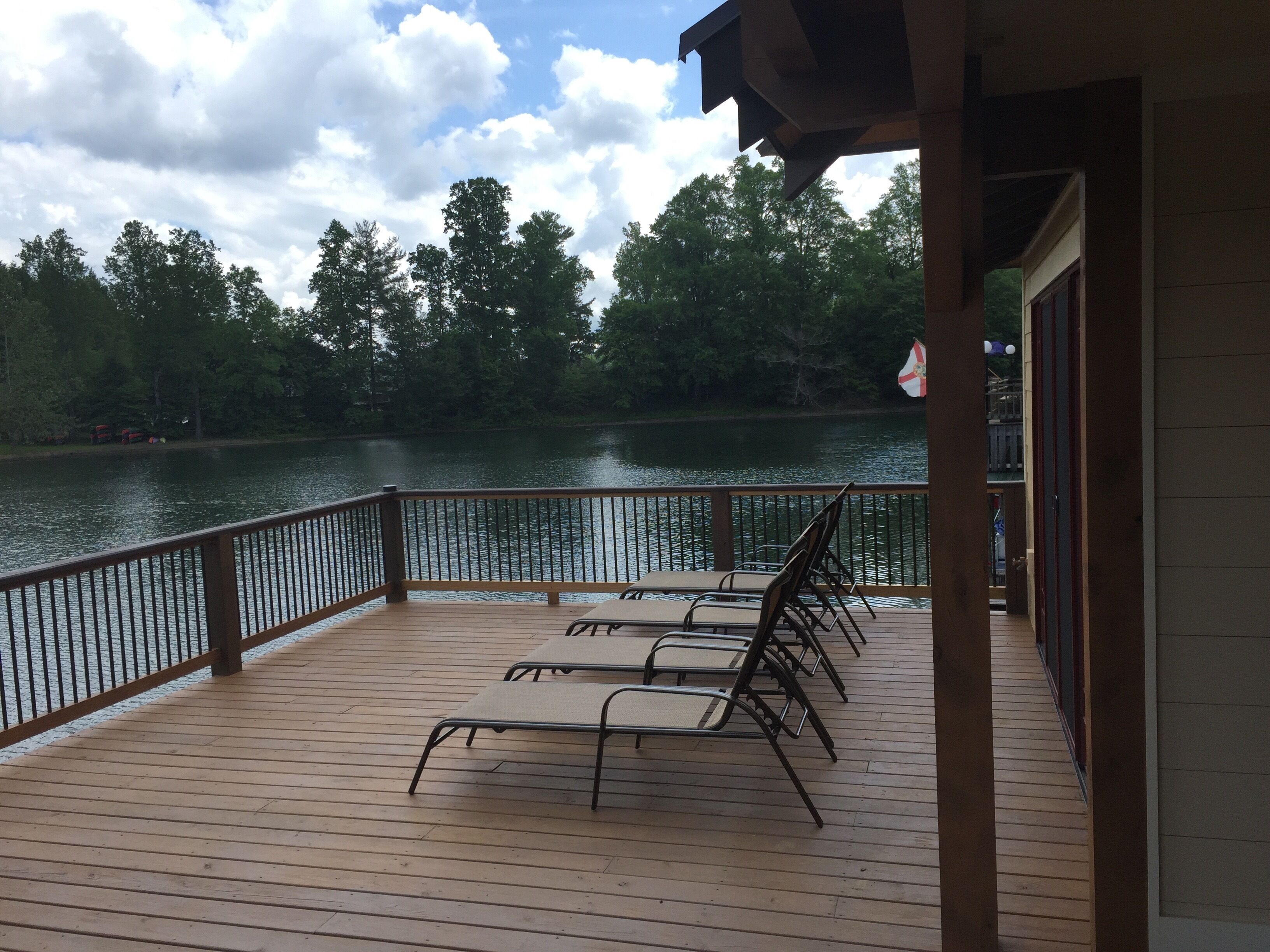 A wooden deck with metal railings overlooking a lake, surrounded by trees.