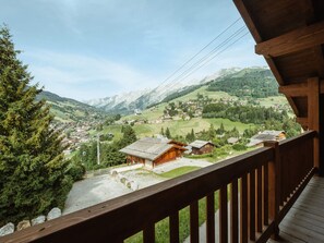 A wooden balcony overlooking a mountainous village with traditional houses and a cable car in the distance.