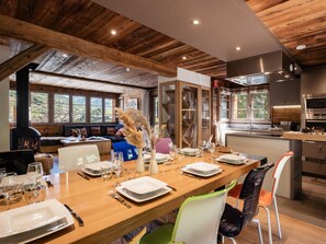 A dining area with a long wooden table set for a meal, a built-in stove, and a kitchen with modern appliances. - 5* Modern Chalet, Near Slopes, Garage, WIFI (La Clusaz)