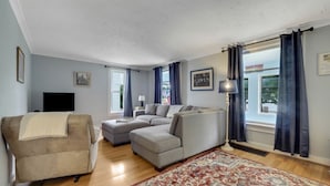 A living room with a beige sofa, a gray sectional, a patterned rug, and a flat-screen TV.
