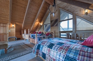 Una habitación de cabaña acogedora con paredes de madera, techo inclinado y ventanas grandes. Hay dos camas con ropa de cama escocesa y un banco.