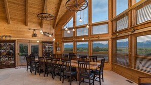 A spacious dining area with a large wooden table and chairs, large windows with blinds, and a rustic ceiling with exposed beams and hanging light fixtures. - Teton Riverfront Retreat | Spacious, Peaceful, Perfect for Family Adventures (Victor)