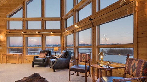 A log cabin interior with large windows, leather chairs, a fur rug, and a table with a lamp. - Teton Riverfront Retreat | Spacious, Peaceful, Perfect for Family Adventures (Victor)
