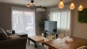 Een woonkamer met een bank, een salontafel, een tv op een standaard, een eettafel met stoelen, en hanglampen.