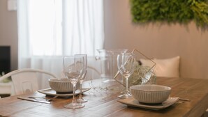 Een eettafel gedekt met witte kommen, borden en wijnglazen, met een groene plant op de achtergrond.