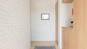 A narrow hallway with white brick walls, a framed picture on the wall, a wooden cabinet with a red sign, and a patterned rug on the floor.