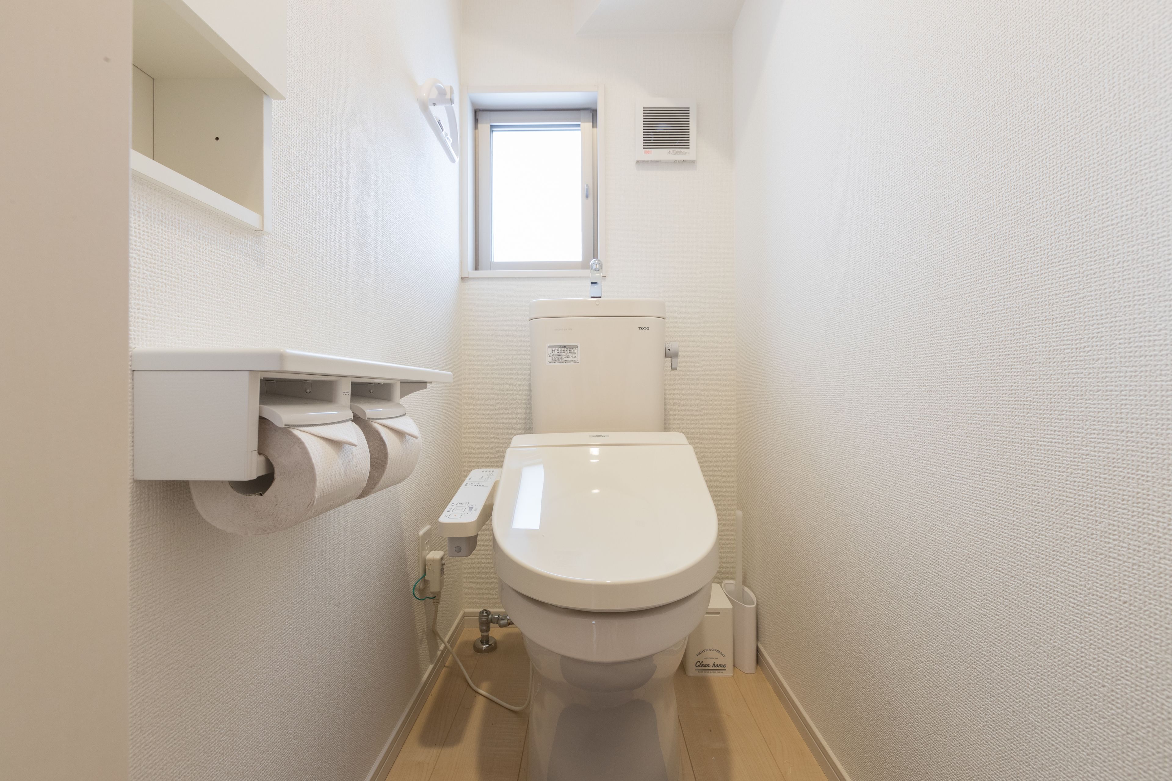 Um banheiro pequeno e branco, com vaso sanitário, rolo de papel higiênico, janela e exaustor.