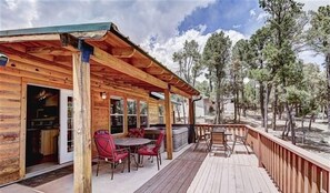 A wooden cabin with a covered patio, red chairs, and a view of trees. - (Alto)