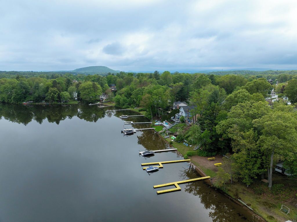 Une propriété au bord du lac, avec des bateaux amarrés, un quai et une maison entourée d’arbres.
