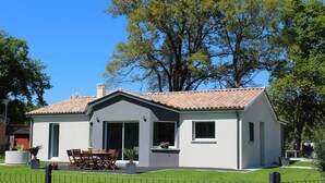 Ein modernes, zweistöckiges Haus mit Ziegeldach, großen Fenstern und einem umzäunten Garten mit Terrassentisch und Stühlen.