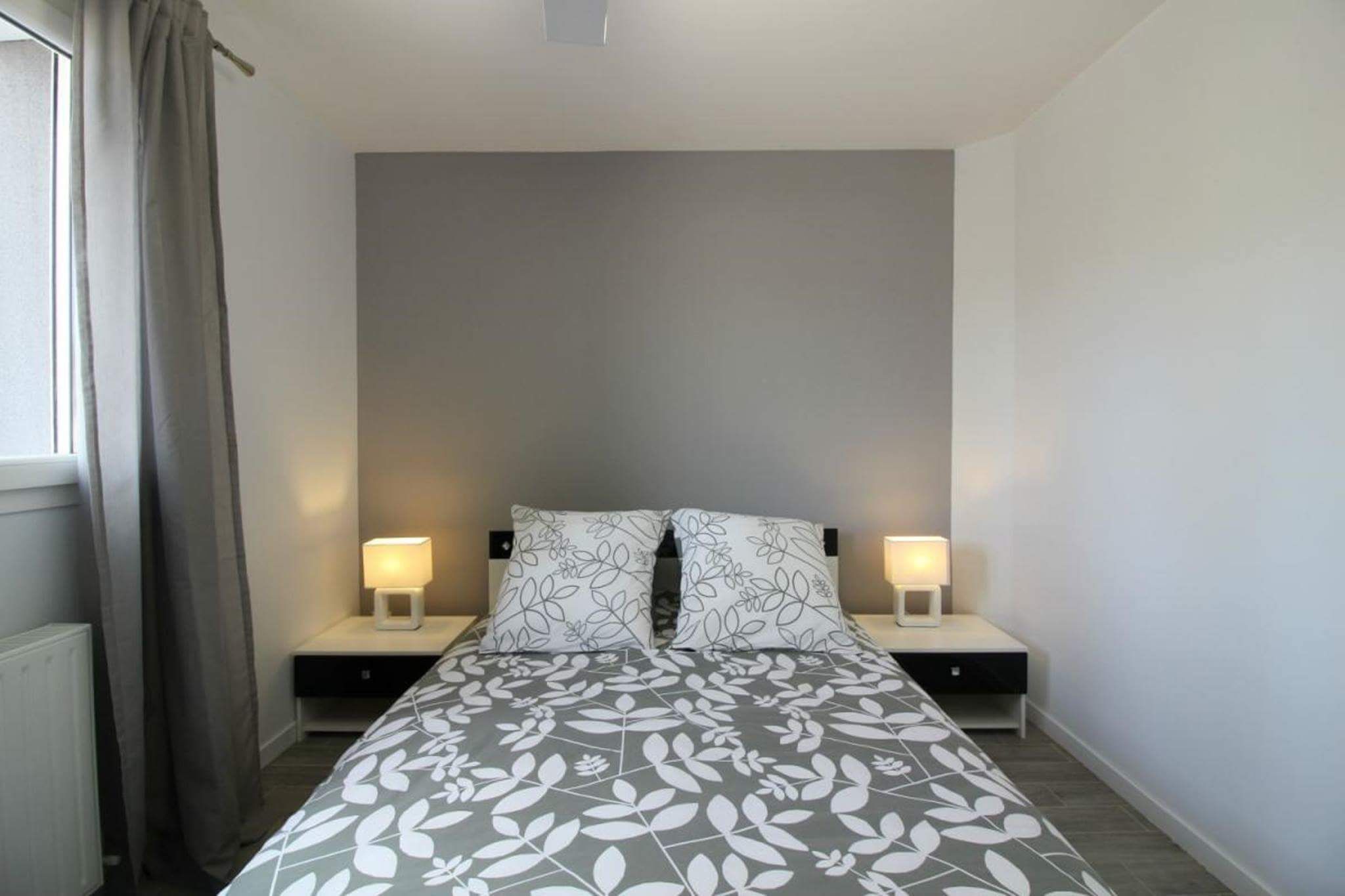A bedroom with a bed, two bedside tables, and a window with curtains.