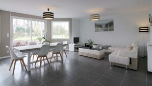 Ein modernes Wohnzimmer mit Essbereich, ausgestattet mit einer Couch, einem Couchtisch, einem Fernseher und einem Esstisch mit Stühlen.