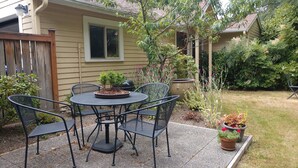 Een terras met een ronde tafel en vier stoelen, omringd door plantenpotten en een houten hek.