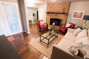 A living room with hardwood flooring, a glass coffee table, a beige sofa, and a red armchair.