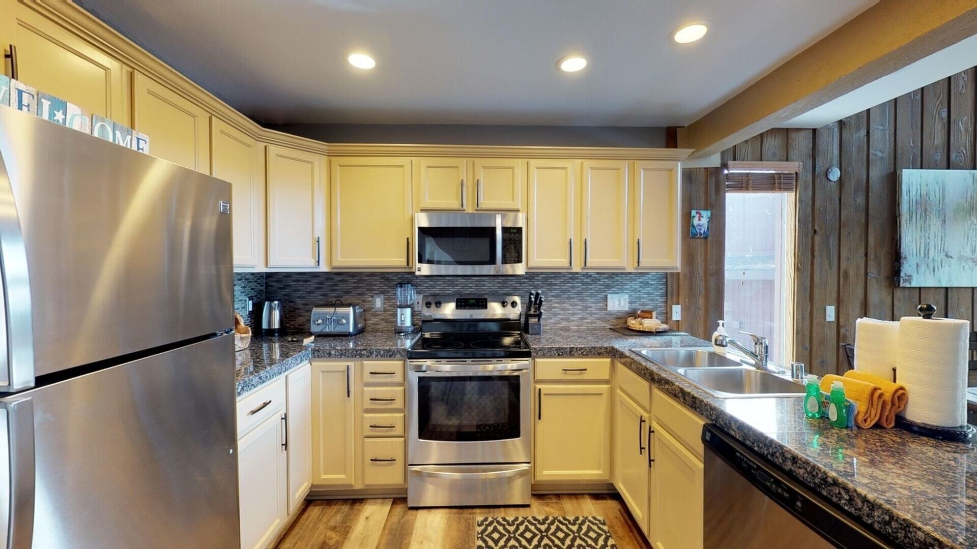A modern kitchen with stainless steel appliances, light-colored cabinets, granite countertops, and a backsplash.