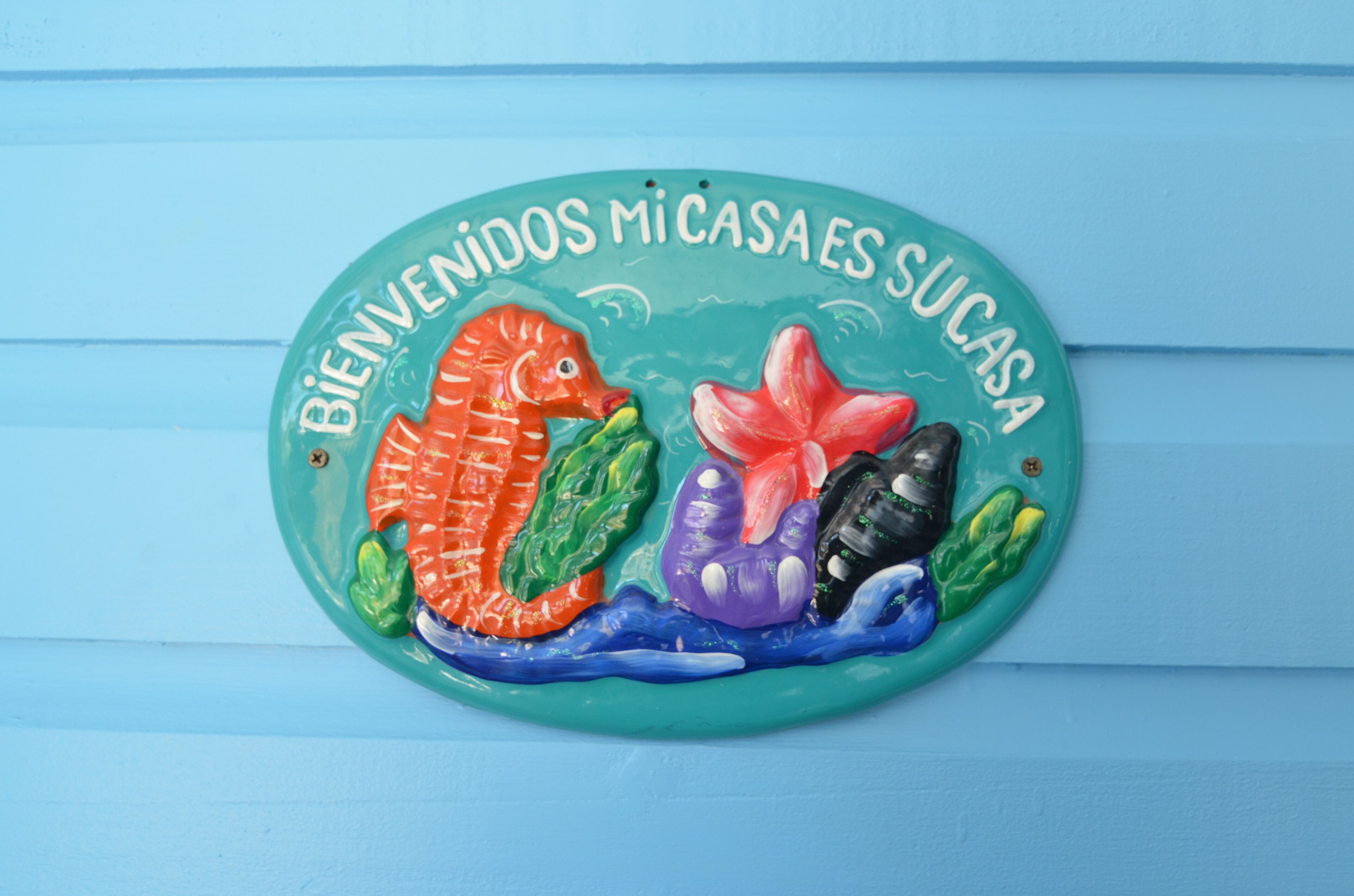 Un azulejo de cerámica con peces de colores y el texto "BIENVENIDOS MI CASA ES SU CASA".